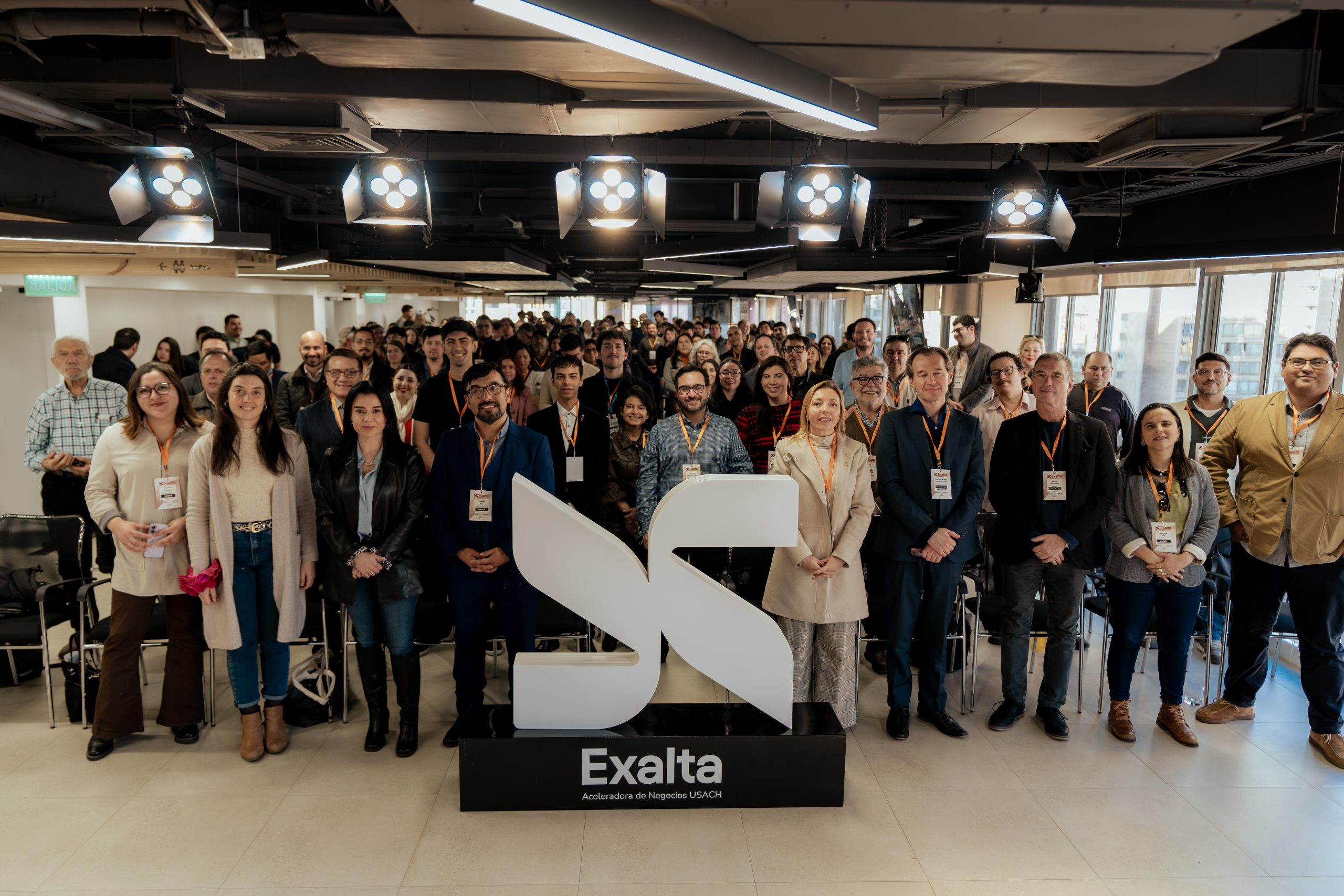 Asistentes al lanzamiento de Exalta, Aceleradora de Negocios Usach, reunidos junto al logotipo de la iniciativa en un encuentro del ecosistema de innovación, ciencia y tecnología.